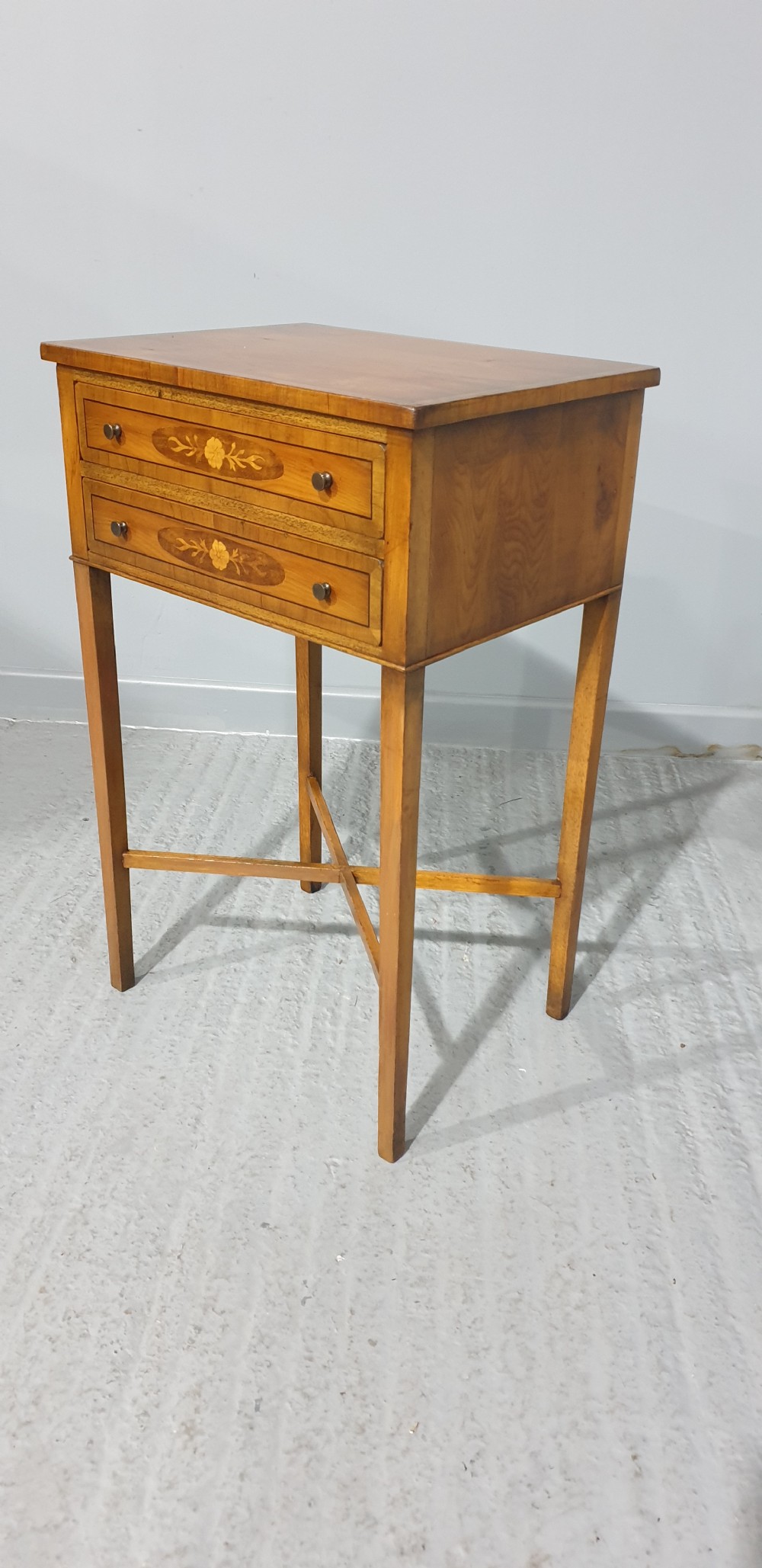 A tall yew wood side table featuring two drawers adorned with oval floral marquetry inlays, slim square legs, and an X-frame stretcher base. View II