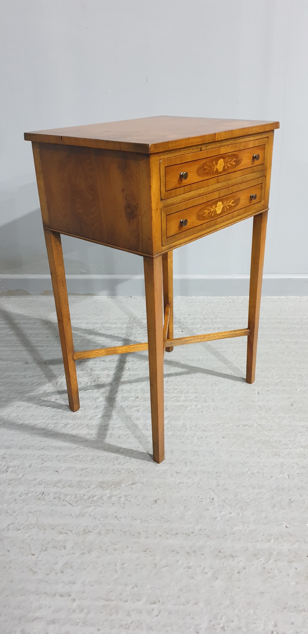 A tall yew wood side table featuring two drawers adorned with oval floral marquetry inlays, slim square legs, and an X-frame stretcher base. View VII