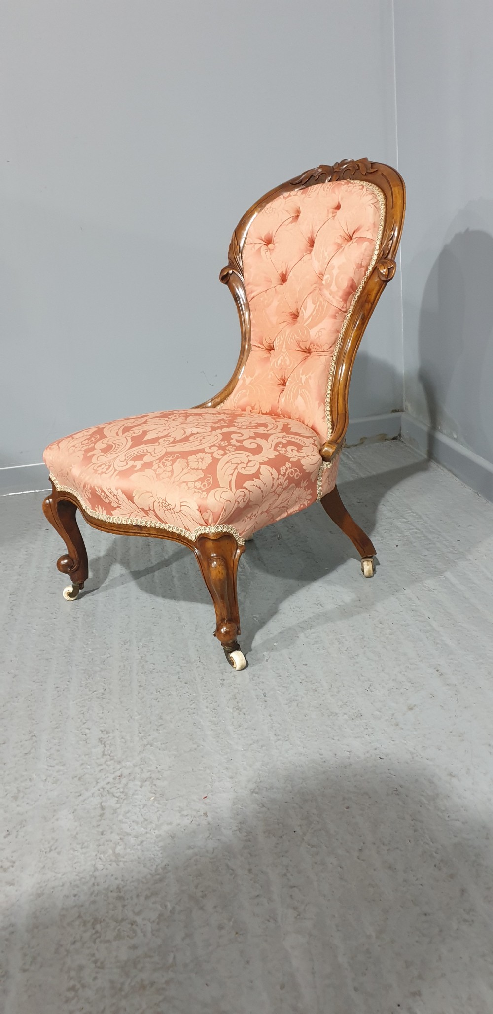 A Victorian mahogany nursing chair with button-backed peach damask upholstery and carved cabriole legs on ceramic castors. View III