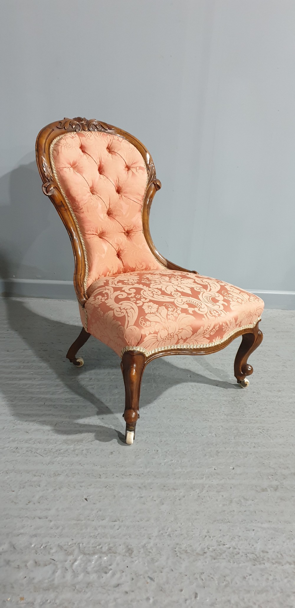 A Victorian mahogany nursing chair with button-backed peach damask upholstery and carved cabriole legs on ceramic castors. View IV