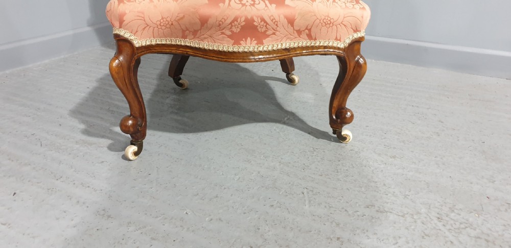 A Victorian mahogany nursing chair with button-backed peach damask upholstery and carved cabriole legs on ceramic castors. View V