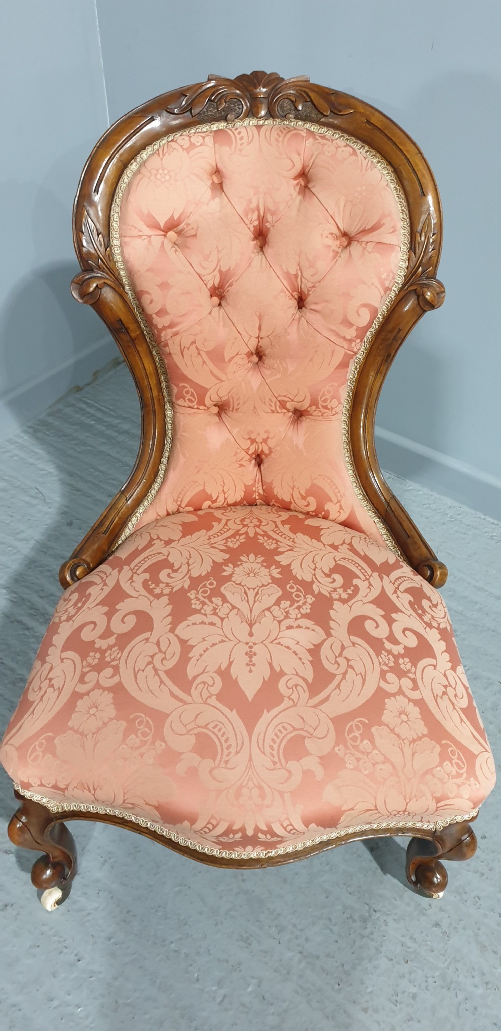 A Victorian mahogany nursing chair with button-backed peach damask upholstery and carved cabriole legs on ceramic castors. View VI