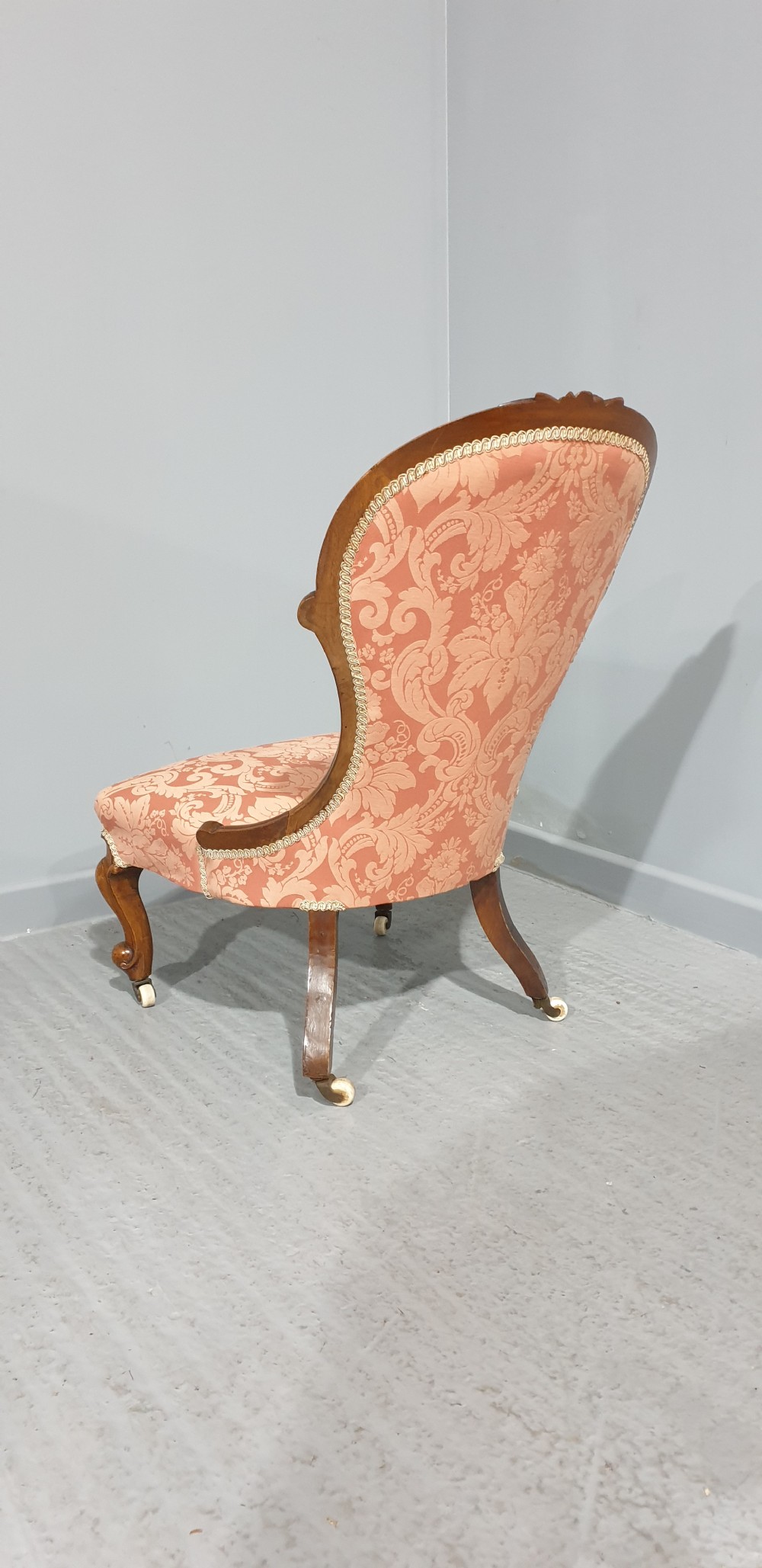 A Victorian mahogany nursing chair with button-backed peach damask upholstery and carved cabriole legs on ceramic castors. View VIII