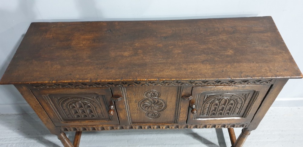A small dark oak carved sideboard with two decorative panelled doors, turned legs, and lower stretchers. View V