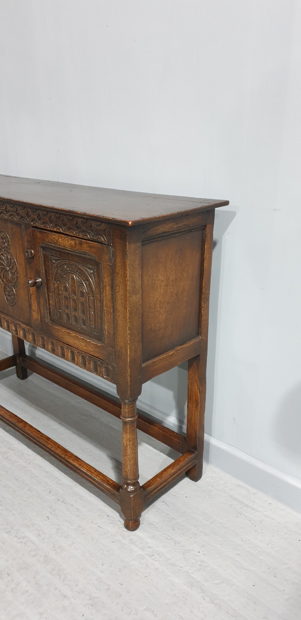 A small dark oak carved sideboard with two decorative panelled doors, turned legs, and lower stretchers. View VI