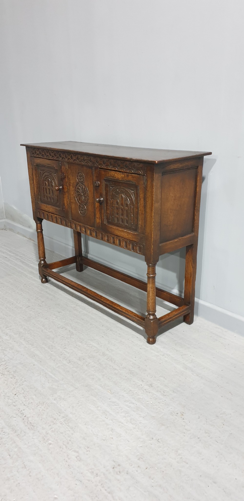 A small dark oak carved sideboard with two decorative panelled doors, turned legs, and lower stretchers. View VII