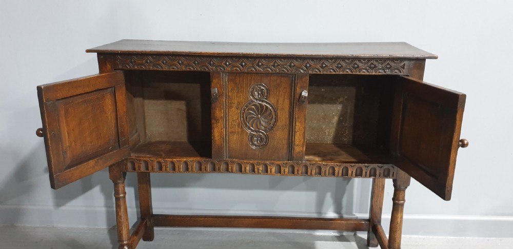 A small dark oak carved sideboard with two decorative panelled doors, turned legs, and lower stretchers. View VIII