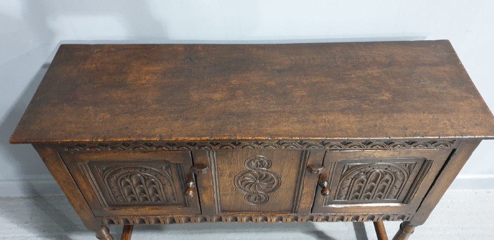 A small dark oak carved sideboard with two decorative panelled doors, turned legs, and lower stretchers. View X