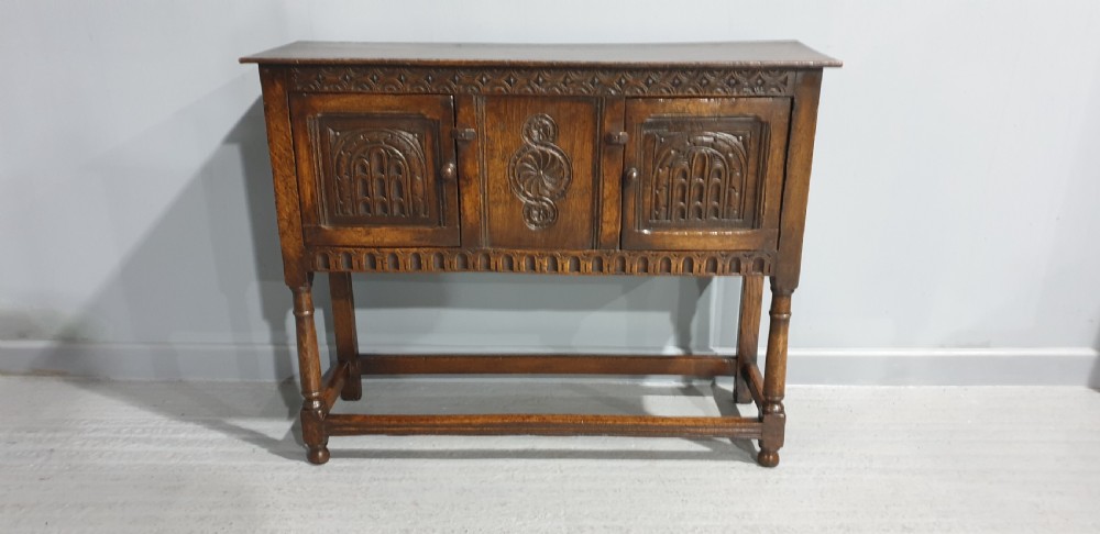 A small dark oak carved sideboard with two decorative panelled doors, turned legs, and lower stretchers. View XI