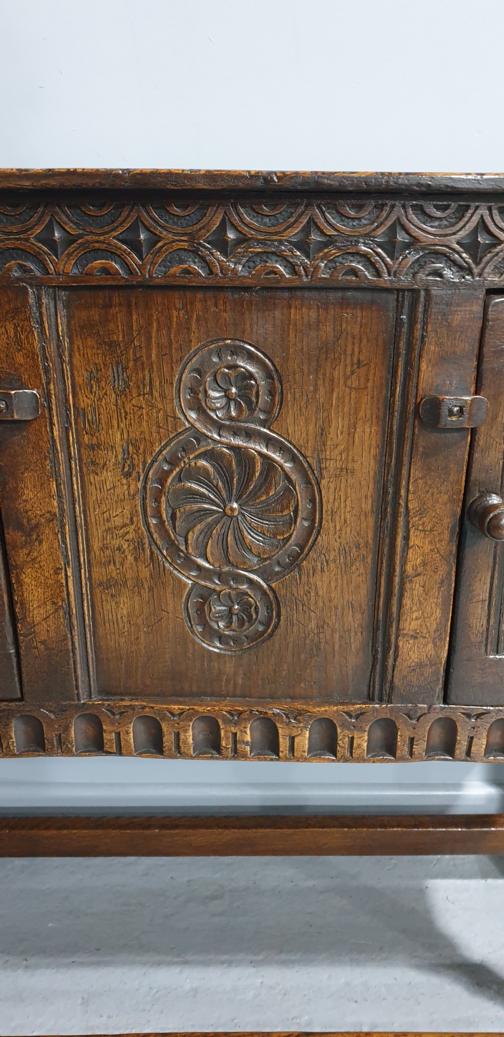 A small dark oak carved sideboard with two decorative panelled doors, turned legs, and lower stretchers. View XII