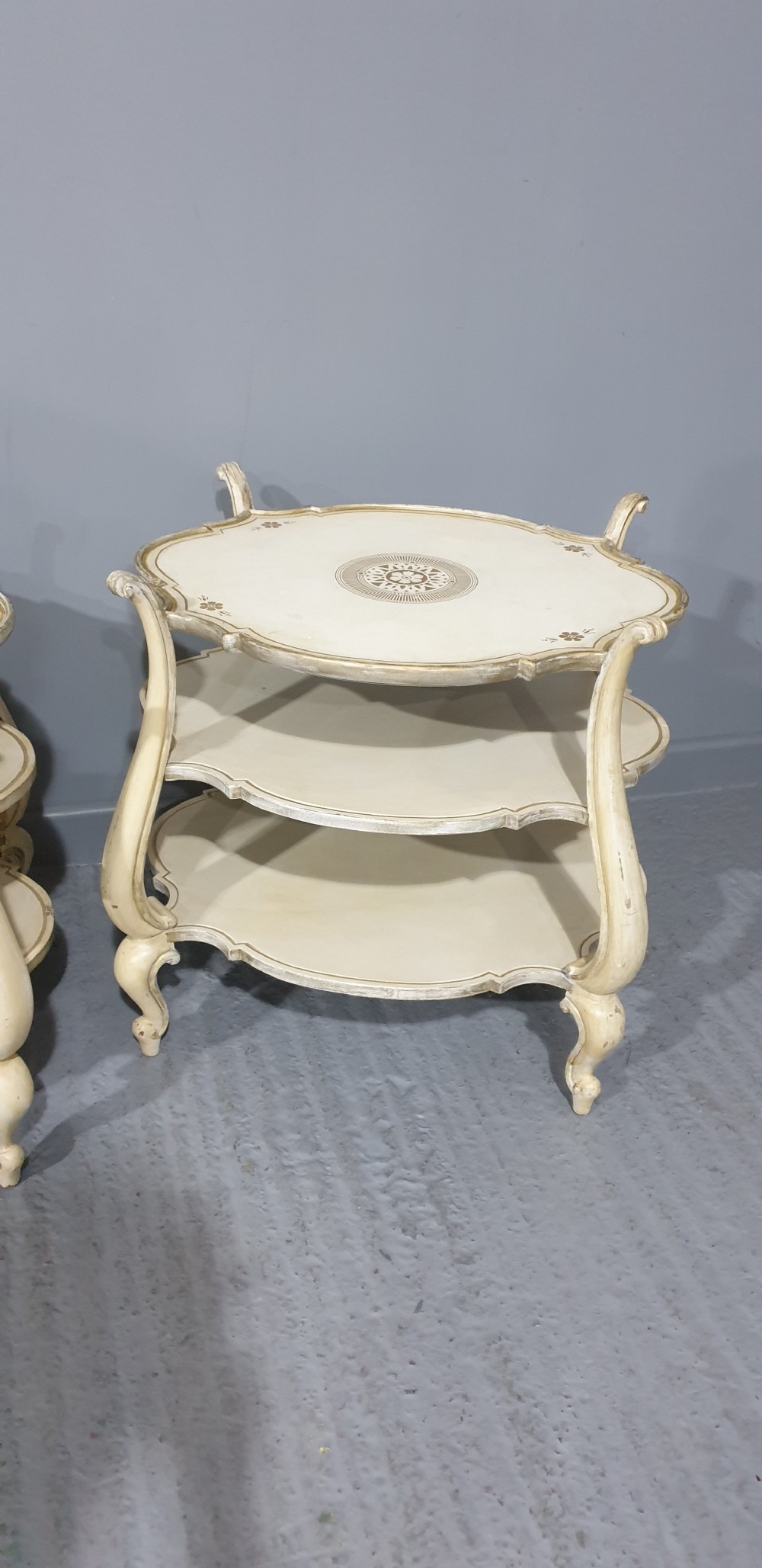 A pair of cream painted three-tier occasional lamp tables with cabriole legs and painted floral medallion tops. View X