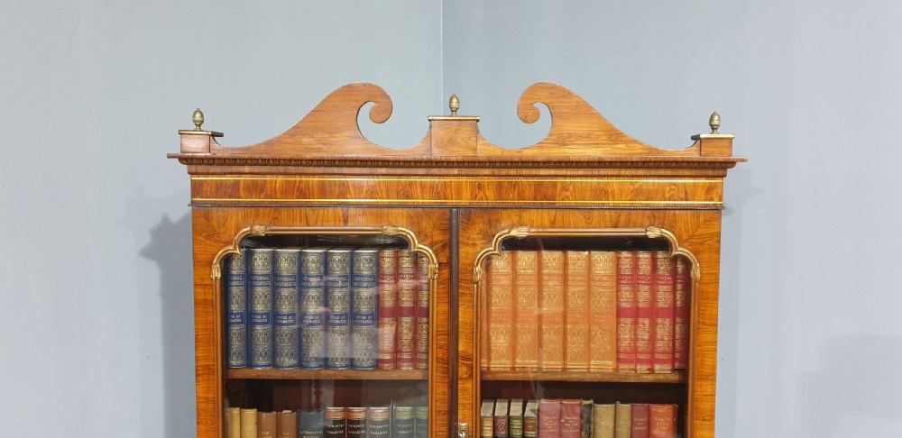A Regency rosewood bureau bookcase featuring a scrolled pediment with brass finials, glazed upper display doors, a roll-top cylinder writing section with brass inlay, and a twin-door lower cupboard. View II