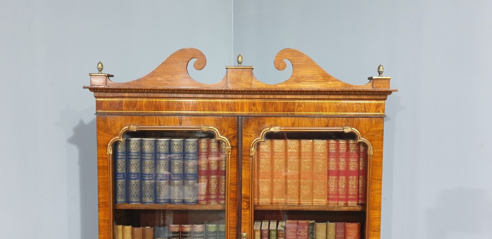 A Regency rosewood bureau bookcase featuring a scrolled pediment with brass finials, glazed upper display doors, a roll-top cylinder writing section with brass inlay, and a twin-door lower cupboard. View III