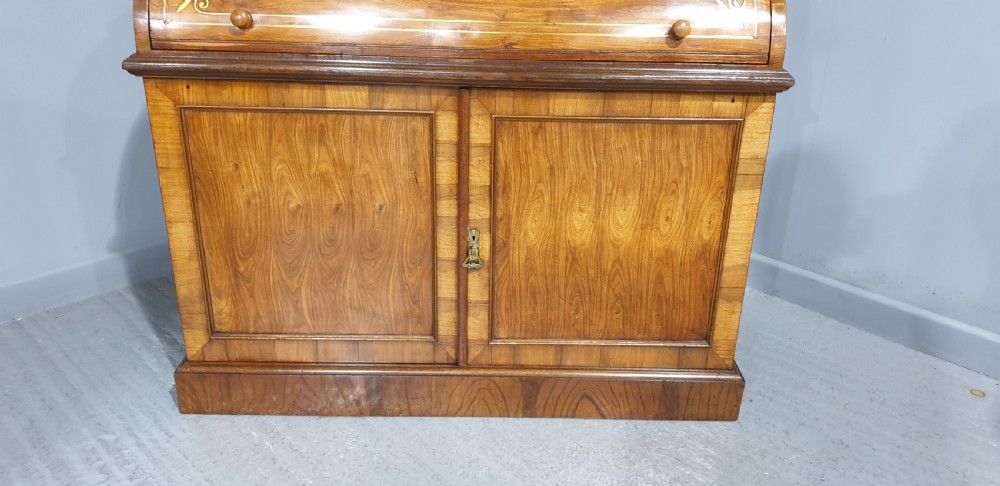 A Regency rosewood bureau bookcase featuring a scrolled pediment with brass finials, glazed upper display doors, a roll-top cylinder writing section with brass inlay, and a twin-door lower cupboard. View VI