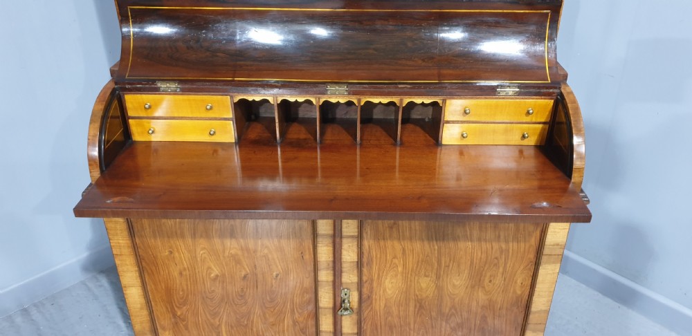 A Regency rosewood bureau bookcase featuring a scrolled pediment with brass finials, glazed upper display doors, a roll-top cylinder writing section with brass inlay, and a twin-door lower cupboard. View X