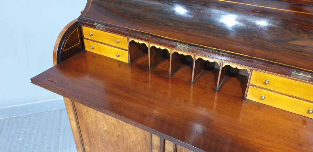 A Regency rosewood bureau bookcase featuring a scrolled pediment with brass finials, glazed upper display doors, a roll-top cylinder writing section with brass inlay, and a twin-door lower cupboard. View XI