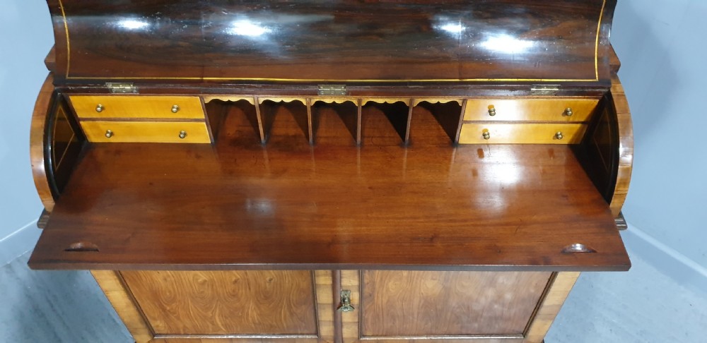 A Regency rosewood bureau bookcase featuring a scrolled pediment with brass finials, glazed upper display doors, a roll-top cylinder writing section with brass inlay, and a twin-door lower cupboard. View XII