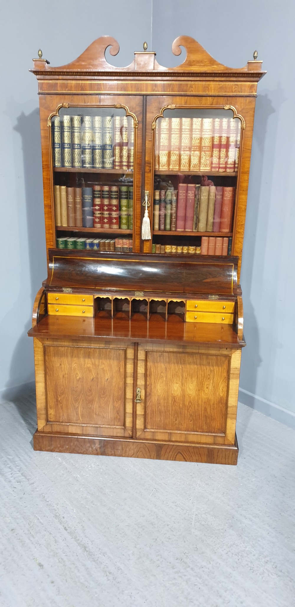 A Regency rosewood bureau bookcase featuring a scrolled pediment with brass finials, glazed upper display doors, a roll-top cylinder writing section with brass inlay, and a twin-door lower cupboard. View XIII
