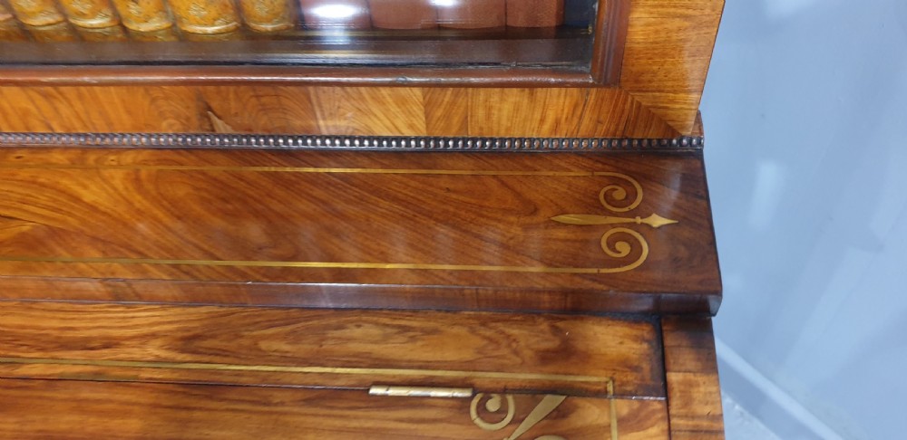 A Regency rosewood bureau bookcase featuring a scrolled pediment with brass finials, glazed upper display doors, a roll-top cylinder writing section with brass inlay, and a twin-door lower cupboard. View XV