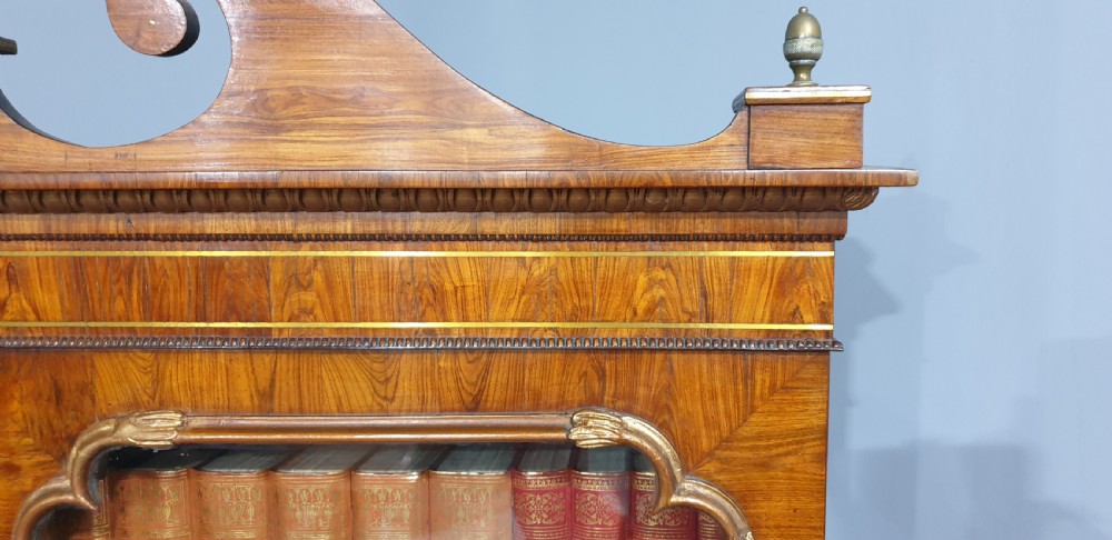 A Regency rosewood bureau bookcase featuring a scrolled pediment with brass finials, glazed upper display doors, a roll-top cylinder writing section with brass inlay, and a twin-door lower cupboard. View XVII