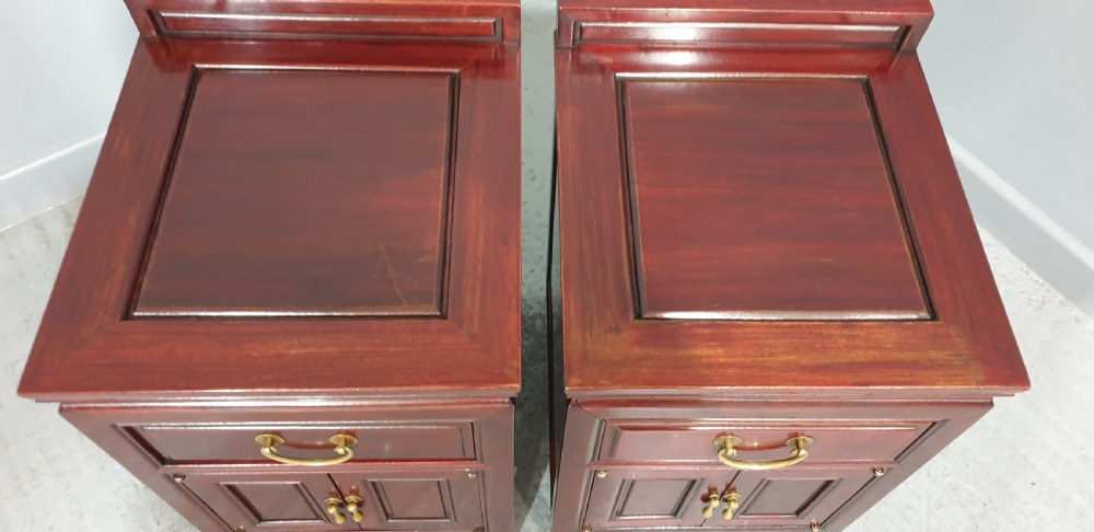 A matching pair of reddish-brown lacquered Oriental bedside cabinets featuring brass handles, single upper drawers, double cupboard doors, and panelled detailing. View II