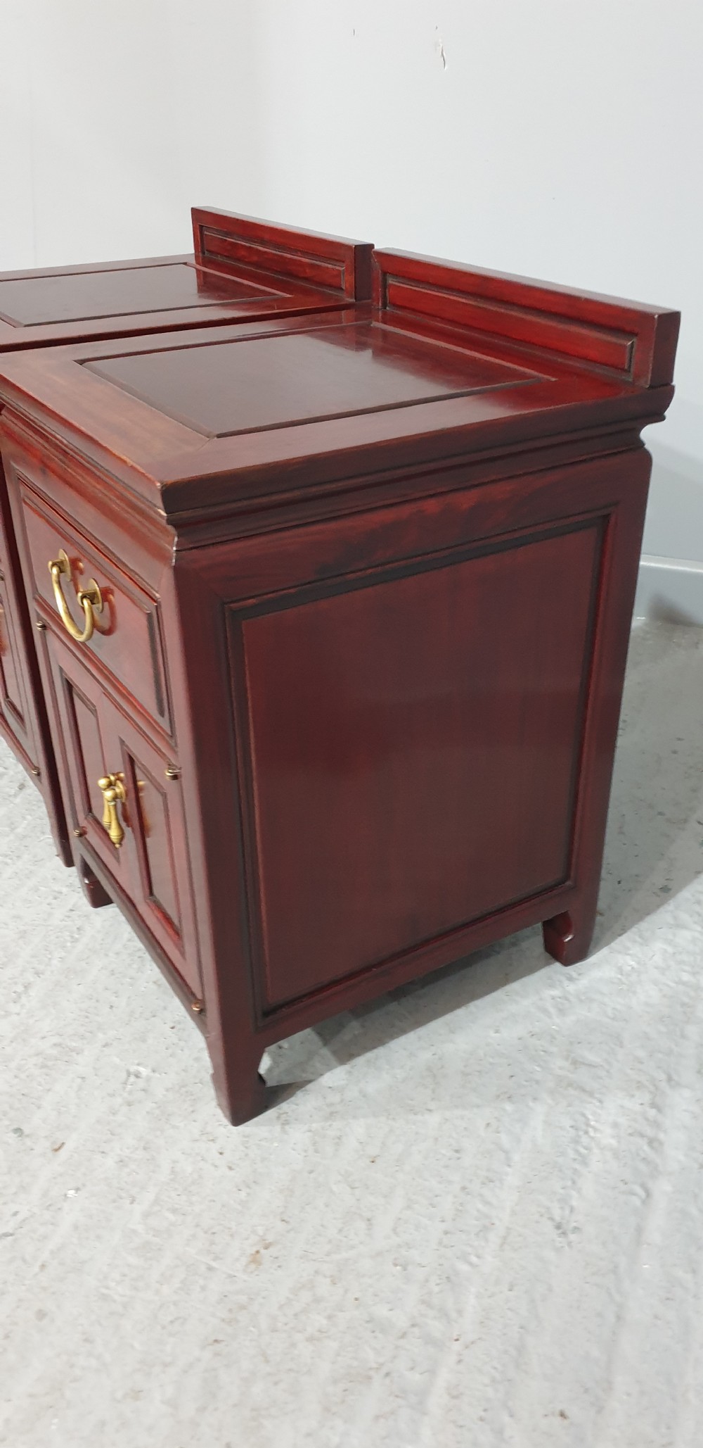 A matching pair of reddish-brown lacquered Oriental bedside cabinets featuring brass handles, single upper drawers, double cupboard doors, and panelled detailing. View III