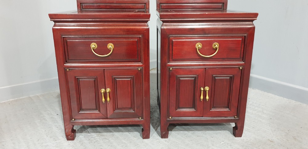 A matching pair of reddish-brown lacquered Oriental bedside cabinets featuring brass handles, single upper drawers, double cupboard doors, and panelled detailing. View V