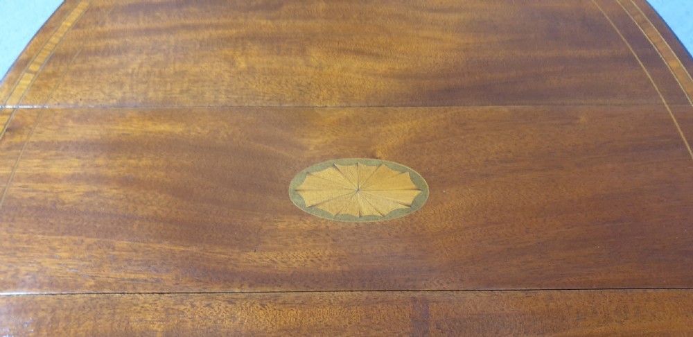 An Edwardian mahogany baby Sutherland drop-leaf table featuring an oval top with satinwood crossbanding, central marquetry patera, slender turned legs, and brass casters. View III