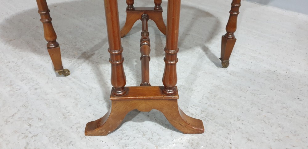 An Edwardian mahogany baby Sutherland drop-leaf table featuring an oval top with satinwood crossbanding, central marquetry patera, slender turned legs, and brass casters. View VI