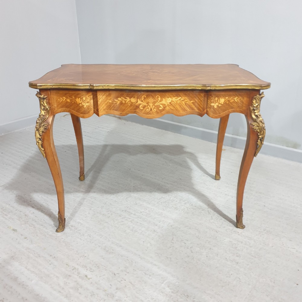 A French Louis XV style bureau plat decorated with floral marquetry inlay, curved cabriole legs, and ornate gilt bronze mounts.