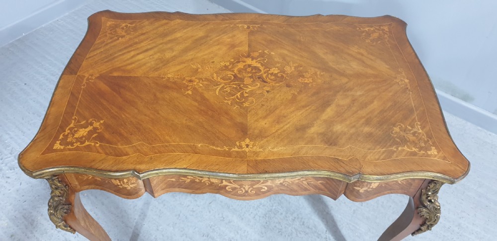 A French Louis XV style bureau plat decorated with floral marquetry inlay, curved cabriole legs, and ornate gilt bronze mounts. View V