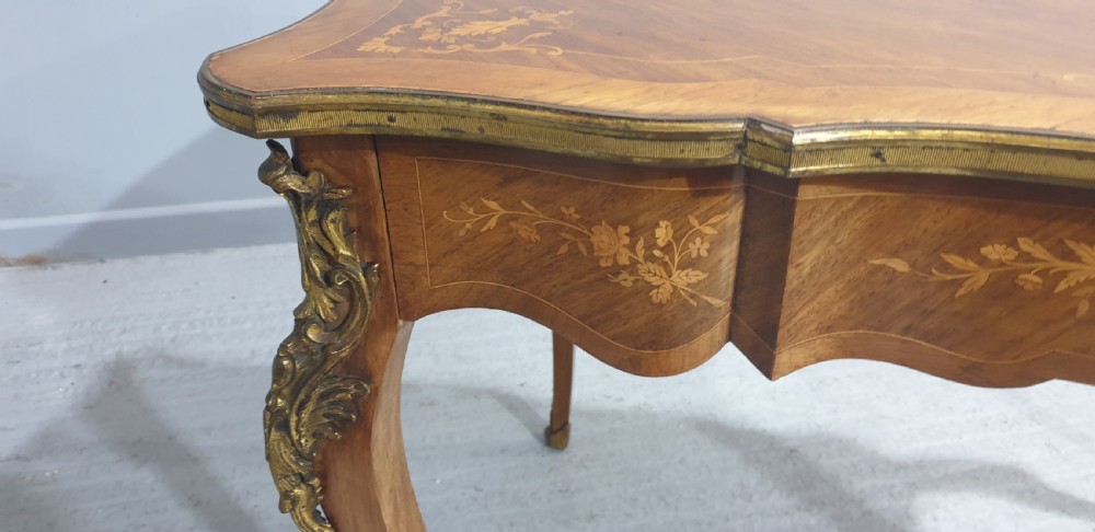 A French Louis XV style bureau plat decorated with floral marquetry inlay, curved cabriole legs, and ornate gilt bronze mounts. View X