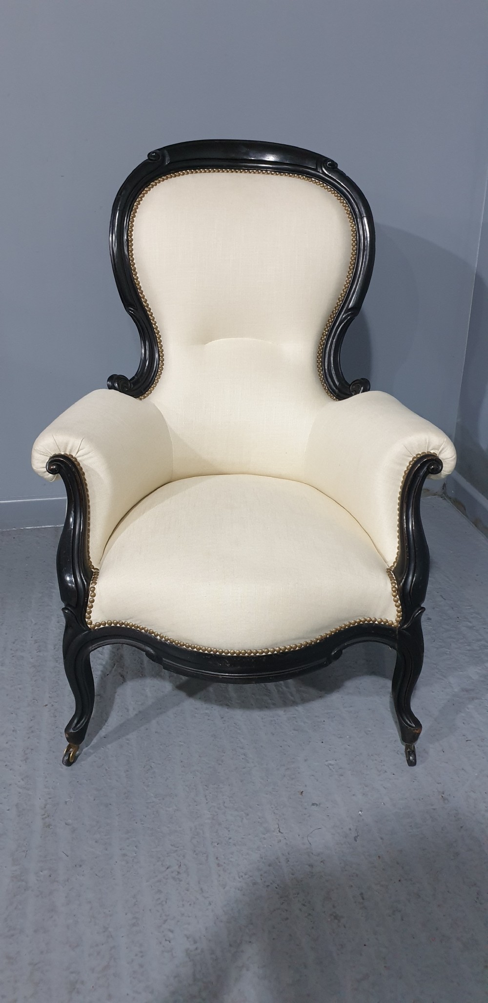 Victorian ebonised spoon-back armchair with off-white upholstery, brass castors, and cabriole legs. View III