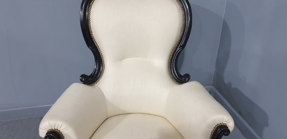 Victorian ebonised spoon-back armchair with off-white upholstery, brass castors, and cabriole legs. View VI