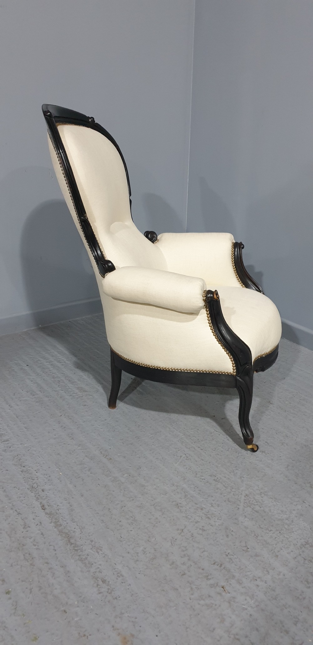 Victorian ebonised spoon-back armchair with off-white upholstery, brass castors, and cabriole legs. View X