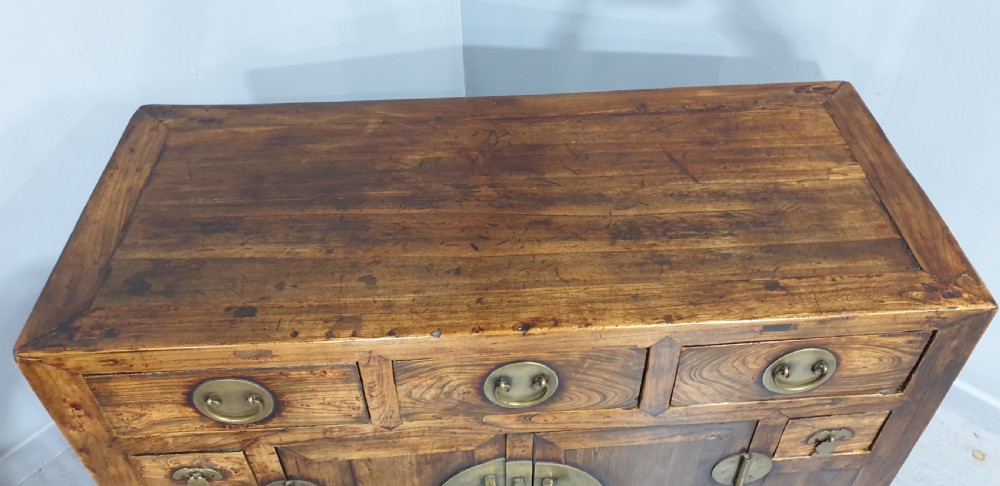 A 19th-century Chinese elm sideboard featuring three upper drawers, two panelled cupboard doors with a central circular brass lockplate, and additional small side drawers with brass fittings. View III