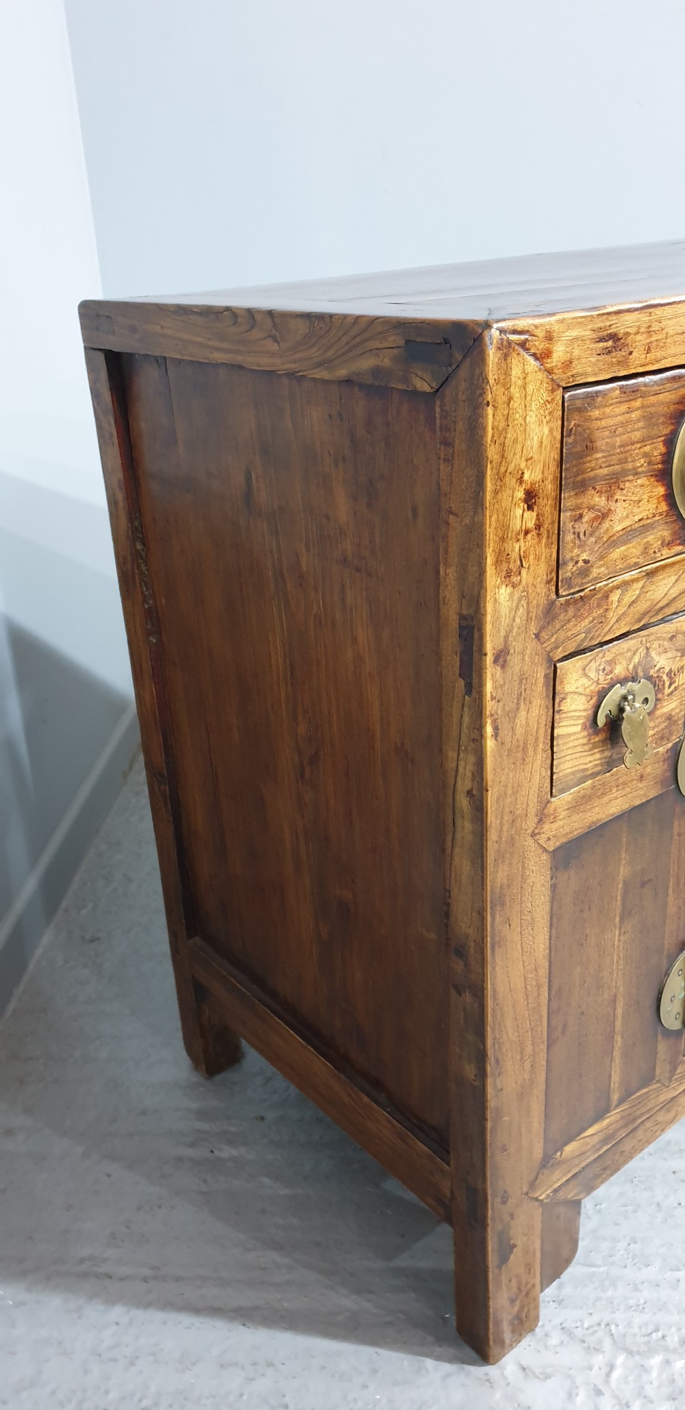A 19th-century Chinese elm sideboard featuring three upper drawers, two panelled cupboard doors with a central circular brass lockplate, and additional small side drawers with brass fittings. View VI