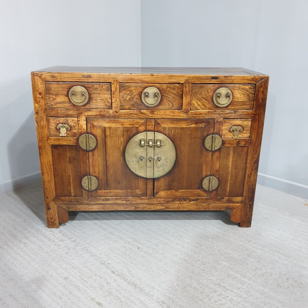 A 19th-century Chinese elm sideboard featuring three upper drawers, two panelled cupboard doors with a central circular brass lockplate, and additional small side drawers with brass fittings.