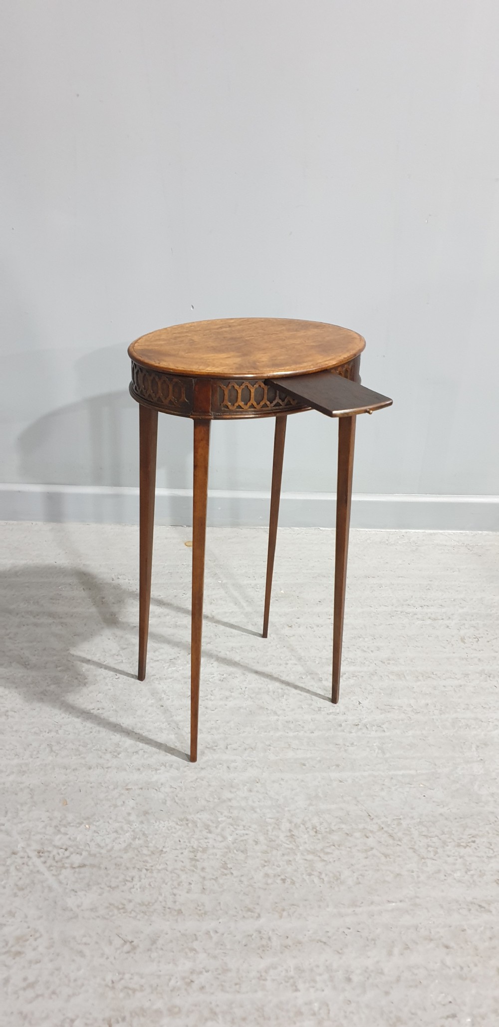 A tall circular mahogany side table featuring a blind fretwork apron and four slender tapered legs. View II