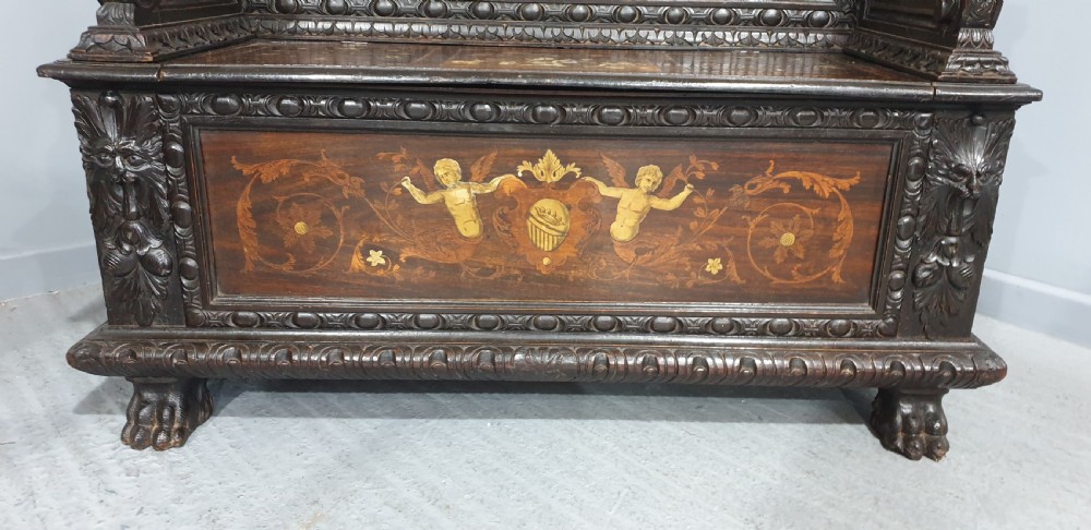 A heavily carved dark walnut Italian hall bench featuring a high backrest with intricate pictorial wood marquetry, winged griffin cresting, and lion paw feet. View V