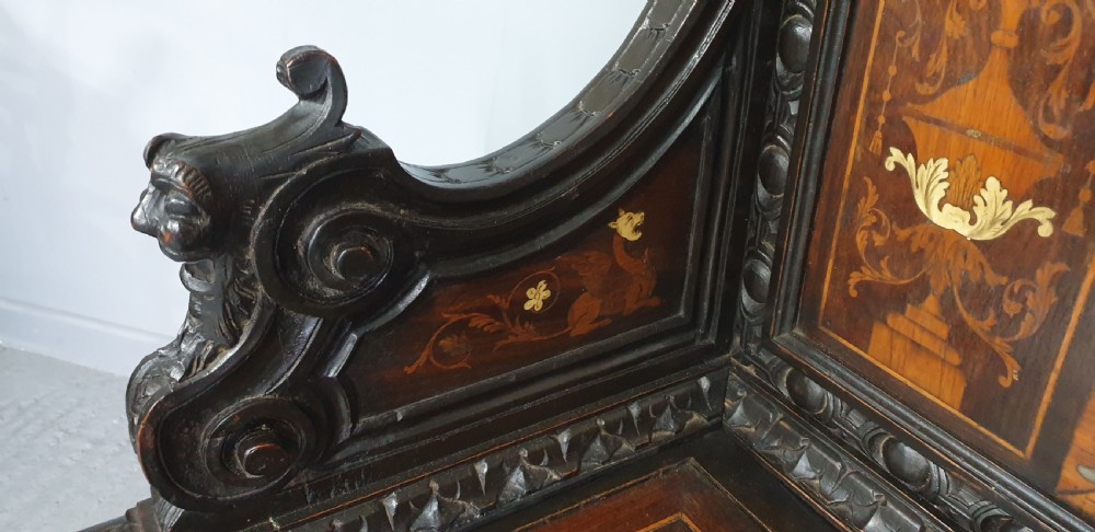 A heavily carved dark walnut Italian hall bench featuring a high backrest with intricate pictorial wood marquetry, winged griffin cresting, and lion paw feet. View VI