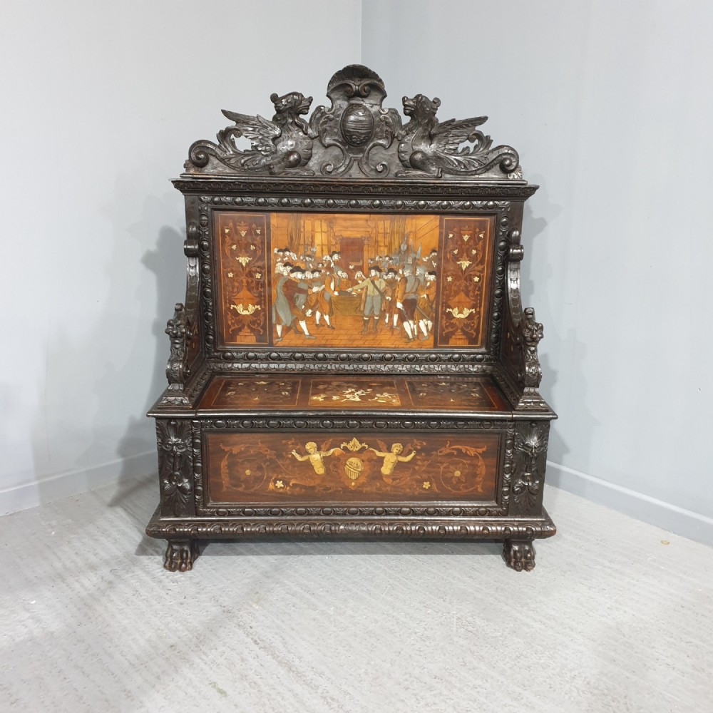 A heavily carved dark walnut Italian hall bench featuring a high backrest with intricate pictorial wood marquetry, winged griffin cresting, and lion paw feet.
