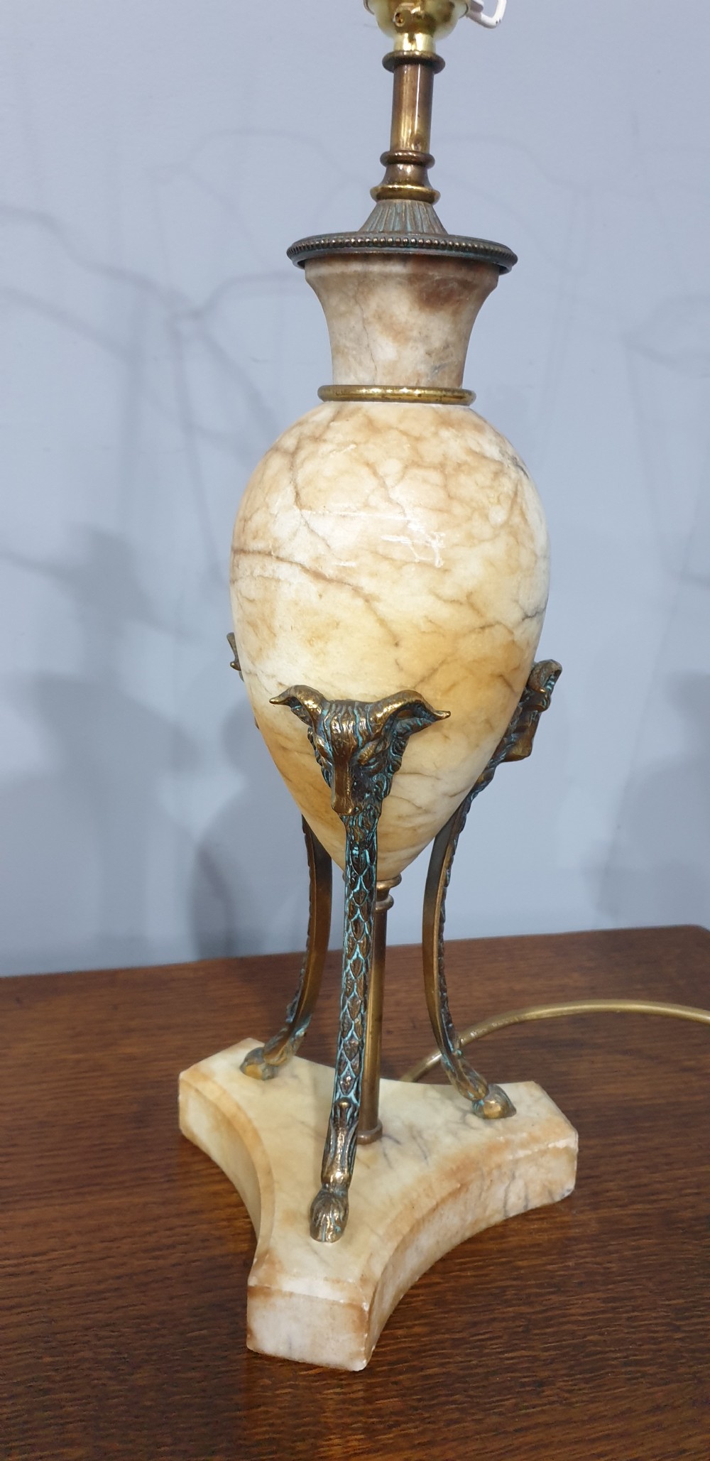 A pair of urn-form alabaster table lamps with brass tripod supports and pleated cream fabric shades resting on a wooden surface. View VI