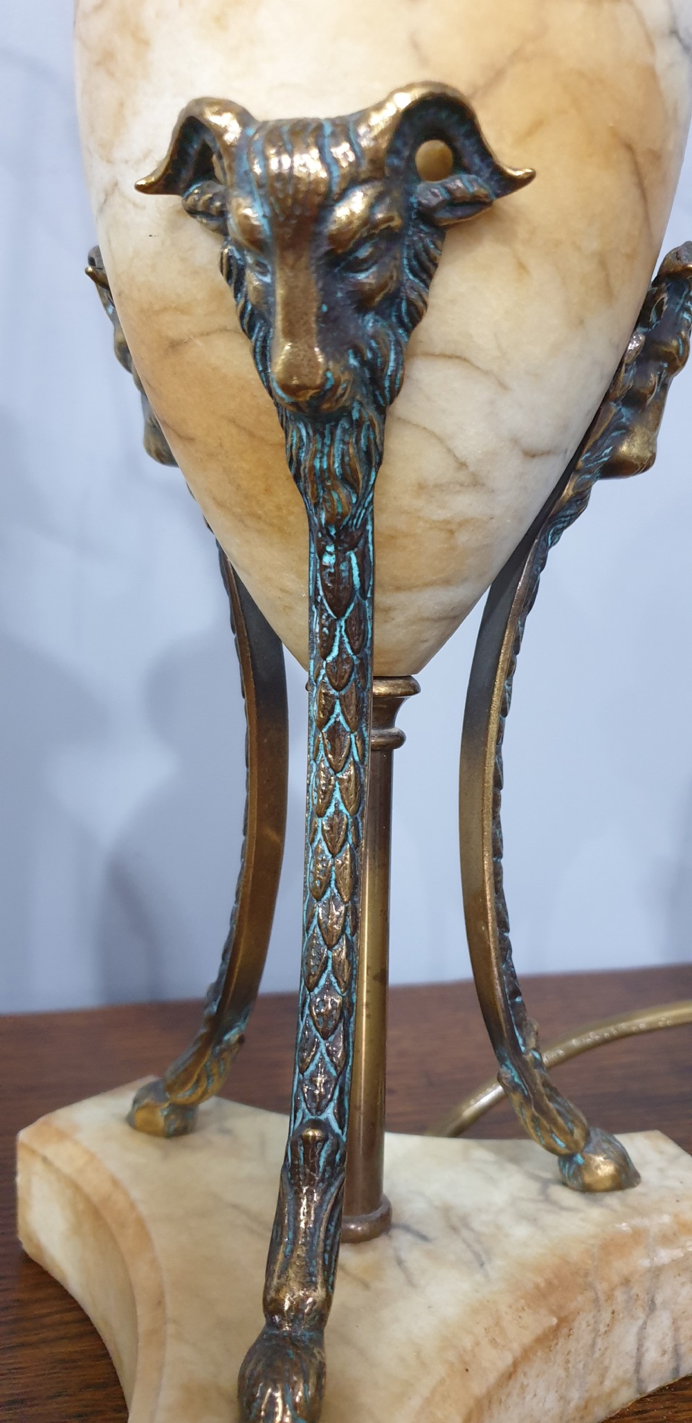A pair of urn-form alabaster table lamps with brass tripod supports and pleated cream fabric shades resting on a wooden surface. View VIII
