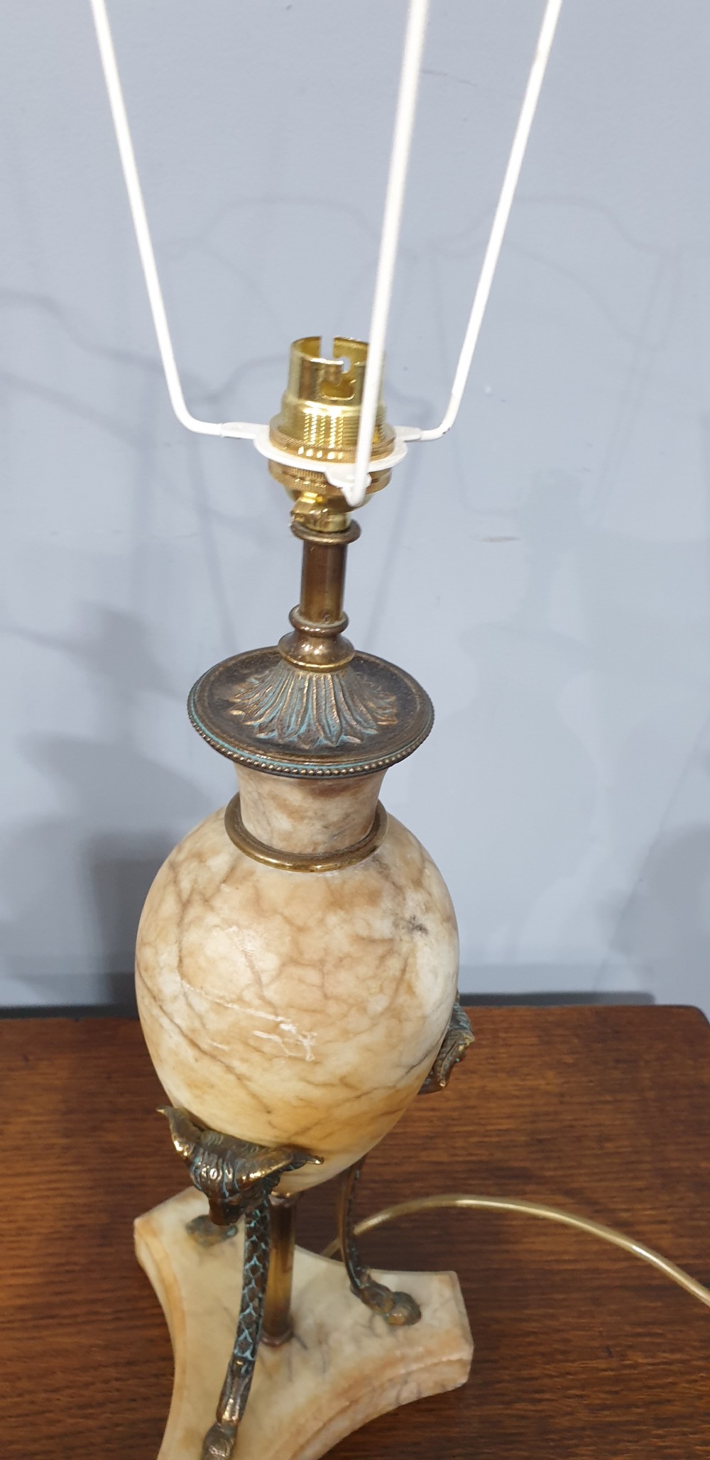 A pair of urn-form alabaster table lamps with brass tripod supports and pleated cream fabric shades resting on a wooden surface. View IX