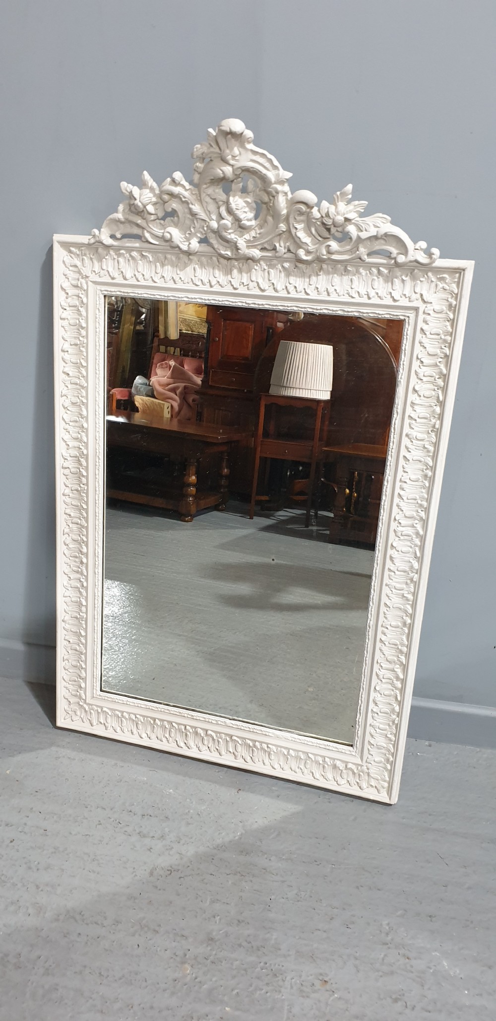 A rectangular off-white painted wall mirror featuring a top carved crest with leaf motifs and a decorative moulded frame. View II