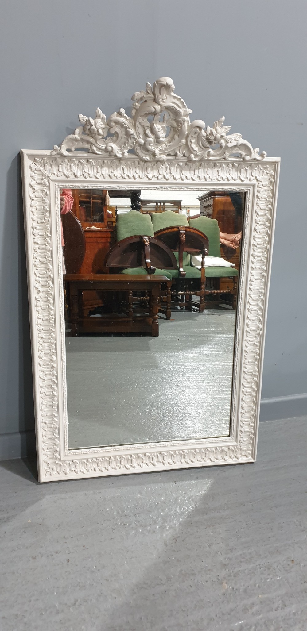 A rectangular off-white painted wall mirror featuring a top carved crest with leaf motifs and a decorative moulded frame. View III