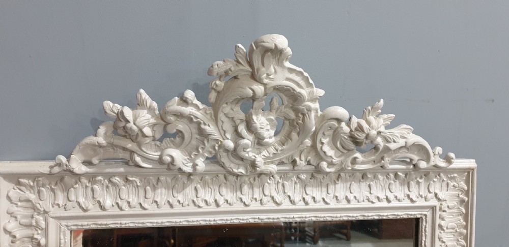 A rectangular off-white painted wall mirror featuring a top carved crest with leaf motifs and a decorative moulded frame. View V