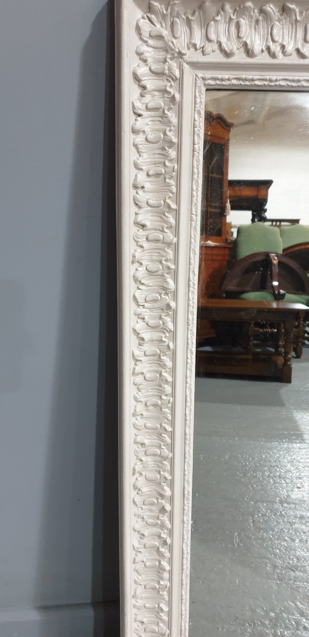 A rectangular off-white painted wall mirror featuring a top carved crest with leaf motifs and a decorative moulded frame. View VI
