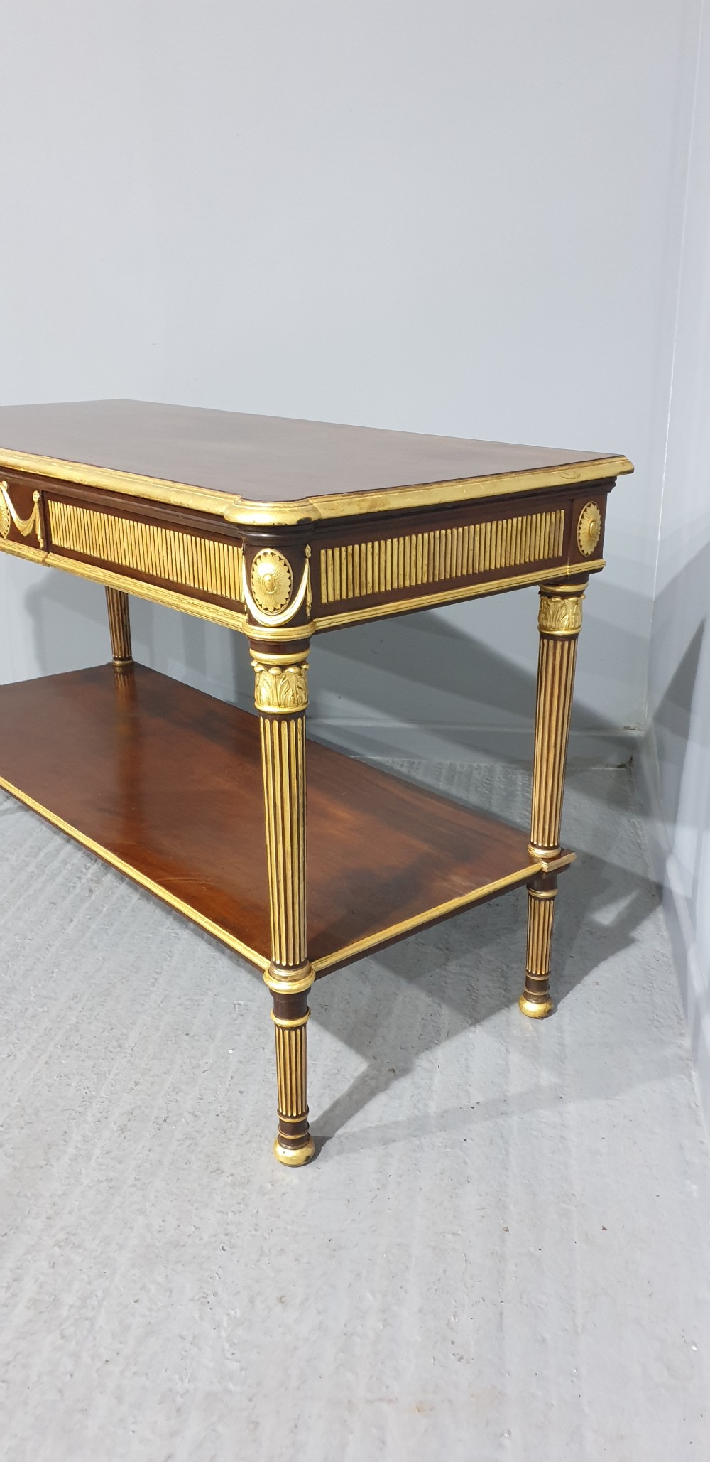 A dark mahogany rectangular console table featuring giltwood fluted legs, a lower shelf, and gold carved swags along the front apron. View III
